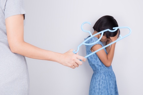 Madre amenazando a su hija pequeña con una percha de plástico