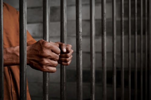 un recluso agarrando las barras de una celda - una condena por incendio imprudente de Código Penal 452 PC puede llevar hasta 6 años de cárcel o prisión