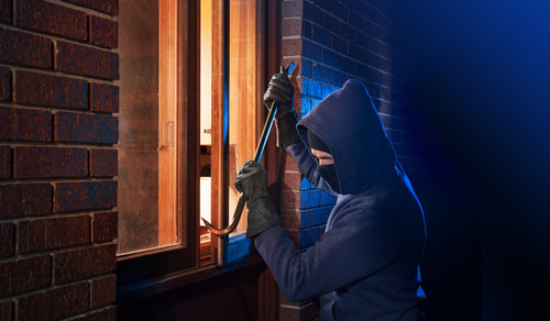 burglar using a crowbar to break in a window