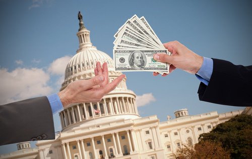 one man handing stack of hundred dollar bills to another man in front of the Capitol Building as an example of embezzlement by a public officer