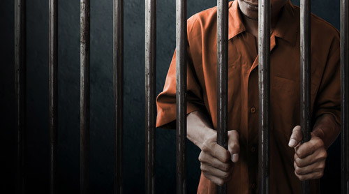un recluso dentro de una celda de la cárcel agarrando las barras - una condena por invasión criminal a la privacidad bajo el Código Penal 647j PC puede llevar hasta 6 meses en la cárcel