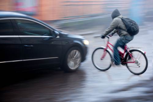car about to hit young man in hoodie on bicycle