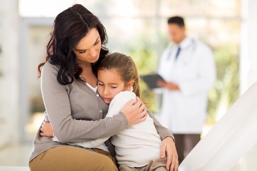 mother comforting sick child with doctor in background