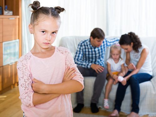 una niña joven mirando celosa mientras sus padres hablan con su hermana