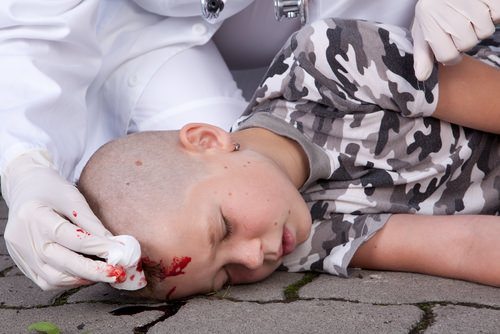 Un niño con una lesión en la cabeza acostado en el suelo mientras un médico lo atiende