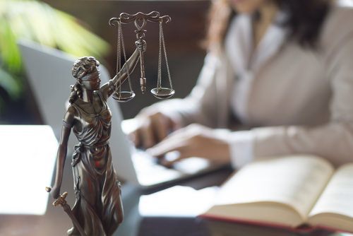 Attorney working on laptop behind scales of justice artpiece