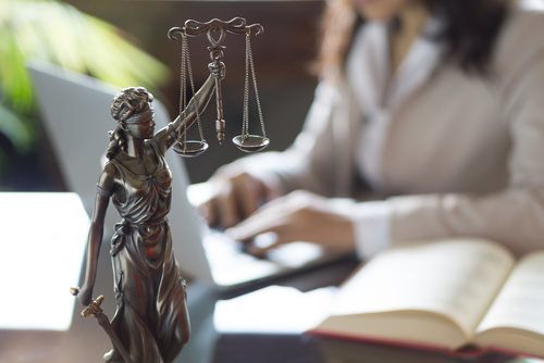 Attorney working on laptop behind scales of justice artpiece