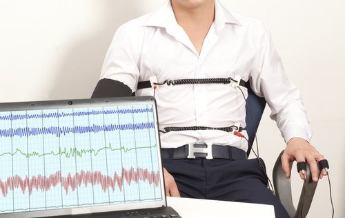 Hombre atado a una máquina de detector de mentiras con los resultados que aparecen en una computadora portátil frente a él