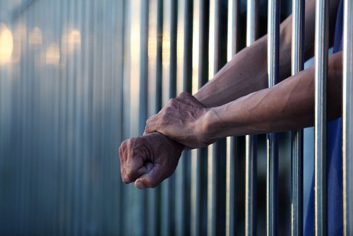 Celda de la cárcel y manos de preso que sobresalen a través de las barras