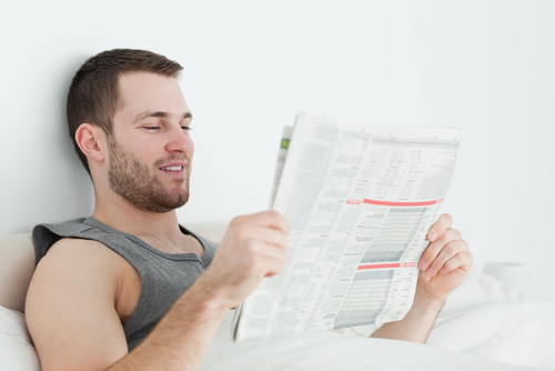 young man reading newspaper in bed