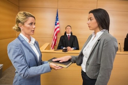 woman in blue suit swearing in young woman on bible as male judge looks on in courtroom