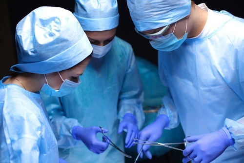 Three people in scrubs and masks performing surgery