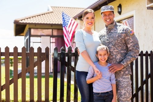soldado masculino de pie con su esposa e hijo fuera de la casa mostrando la bandera de los EE. UU.