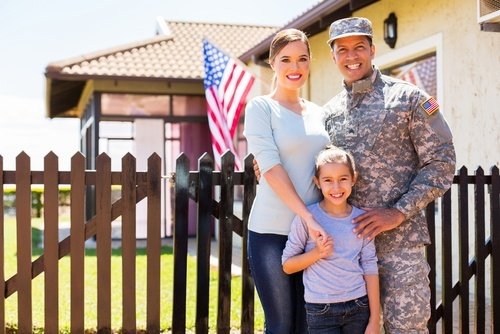 male soldier standing with his wife and child outside house displaying the U.S. flag