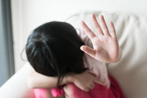 scared little girl with head on her knees and palm out in a "stop" gesture