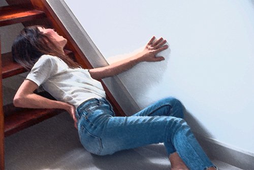 una mujer agarrando su parte baja de la espalda en la parte inferior de una escalera - los accidentes en escaleras a menudo conducen a reclamos de responsabilidad por el lugar en California