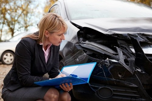 una ajustadora de seguros femenina inspeccionando un automóvil dañado