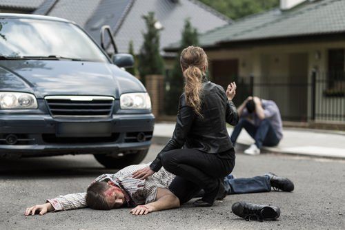 una mujer atendiendo a un hombre herido que yace en la calle después de haber sido golpeado por un vehículo
