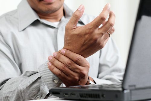 man at laptop clutching his wrist as an example of a workers' compensation carpel tunnel injury