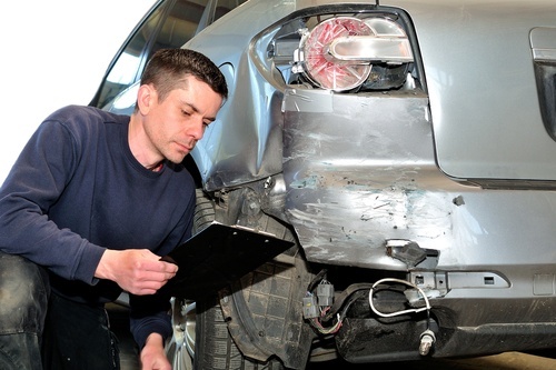 insurance adjuster examining car in body shop