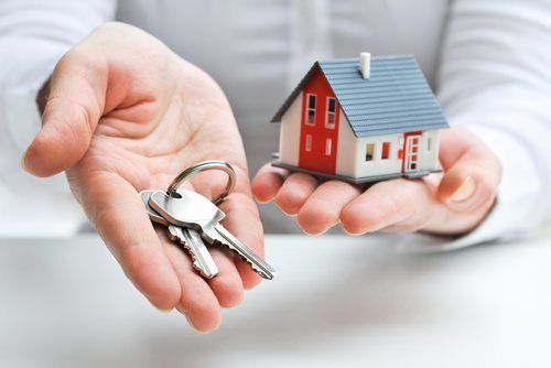 una mano sosteniendo llaves y la otra mano sosteniendo una casa modelo