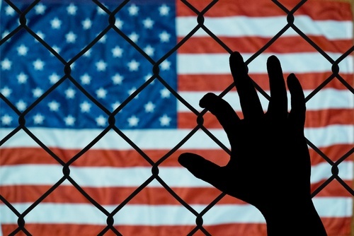 hand against chain-link fence with American flag on the other side