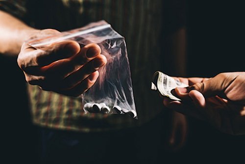 hombre entregando una bolsa de píldoras a cambio de dinero como ejemplo de venta de una sustancia controlada según el Código de Salud y Seguridad de California 11352 HS