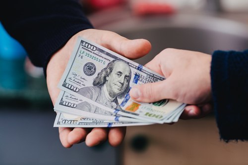 primer plano de una mano poniendo tres billetes de cien dólares en la mano de otra persona