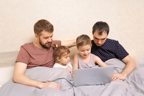 Pareja del mismo sexo masculino jugando en la cama con sus dos hijos pequeños