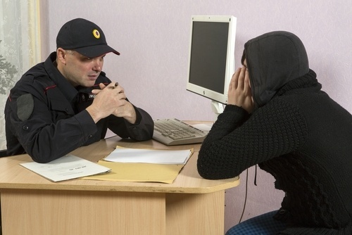 Police officer questioning a young man in a hoodie at a desk