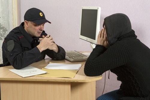 Police officer questioning a young man in a hoodie at a desk