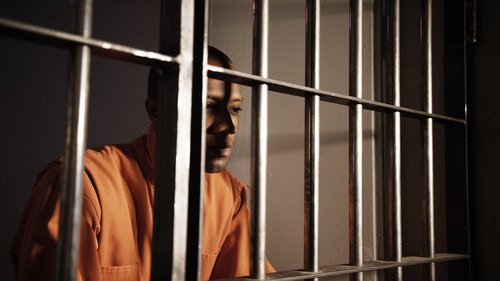 un recluso mirando desde una celda de prisión - una condena por el Código Penal 245a4 PC conlleva hasta 4 años de prisión o cárcel