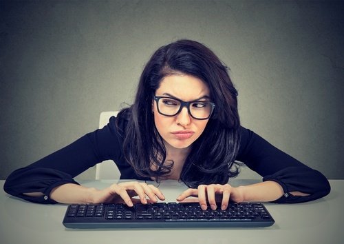 Woman in glasses squinting and leaning forward over a computer keyboard