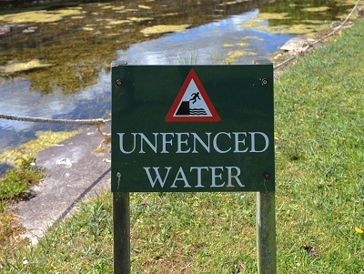 sign reading "unfenced water" next to paved canal.