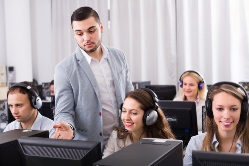 jefe masculino en traje supervisando a recepcionistas con auriculares