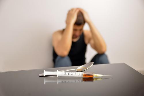 man slumped behind a table with a heroin needle