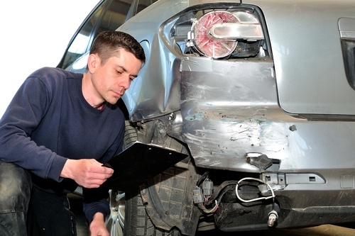 hombre con bloc de notas examinando coche destrozado