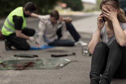 woman on phone while injured pedestrian in background following an accident