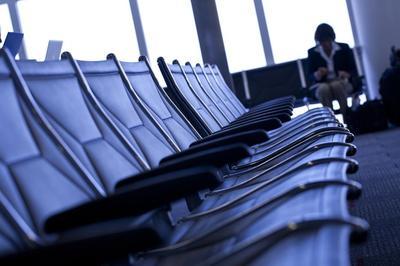Fila de asientos de aeropuerto vacíos con una sola persona sentada en la distancia mirando hacia abajo