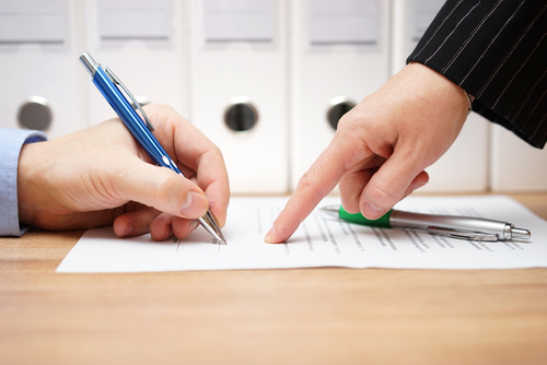 man's hand signing an agreement as another man in suit points where to sign