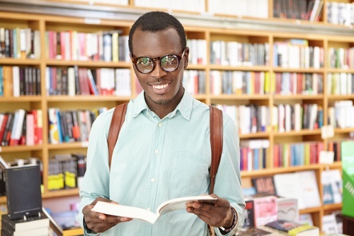 African American teenager with open book in front of a library bookshelf
