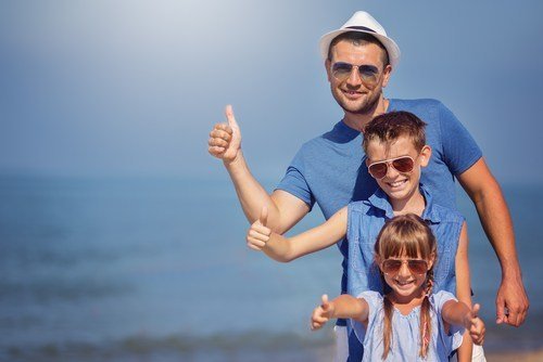 hombre, niño pequeño y niña pequeña levantando el pulgar y sonriendo mientras están al aire libre usando gafas de sol