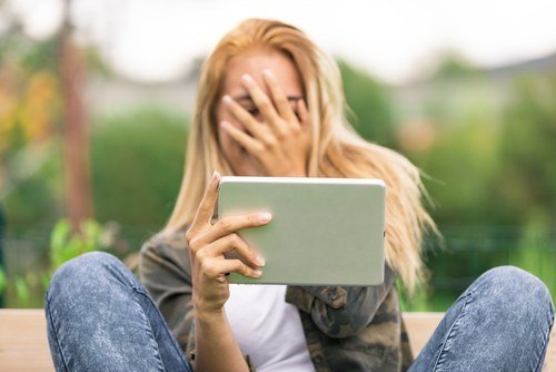 woman looking at a tablet and covering her face with her hand