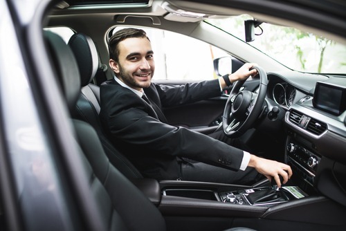 joven hombre con traje detrás del volante de un vehículo con expresión de bienvenida - El Código de Vehículos 23152 e VC establece un límite de BAC más bajo para los conductores de compartición de viajes