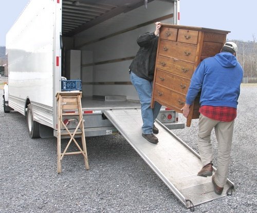 Two men carrying a chest of drawers into a moving van
