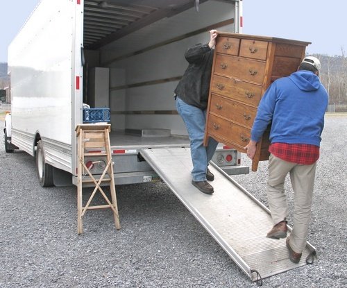 Dos hombres llevando un cofre de cajones a una camioneta de mudanzas