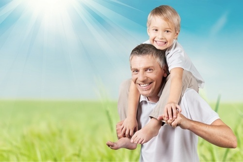 smiling father with young son on his shoulders on a sunny day