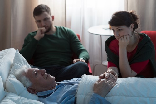 joven hombre y mujer sentados en la sala de hospital preocupados por el hombre mayor que está acostado en la cama del hospital