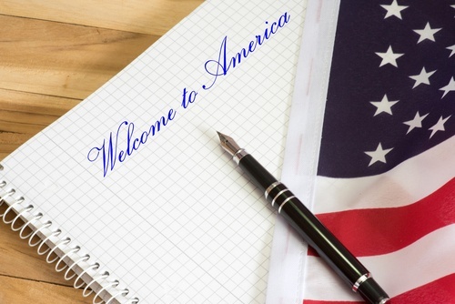 pluma sobre bandera y cuaderno que dice "Bienvenido a América"