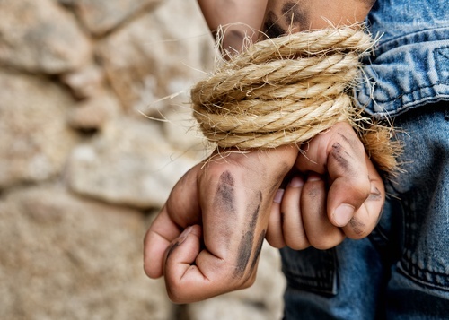man's dirty hands bound with rope behind his back